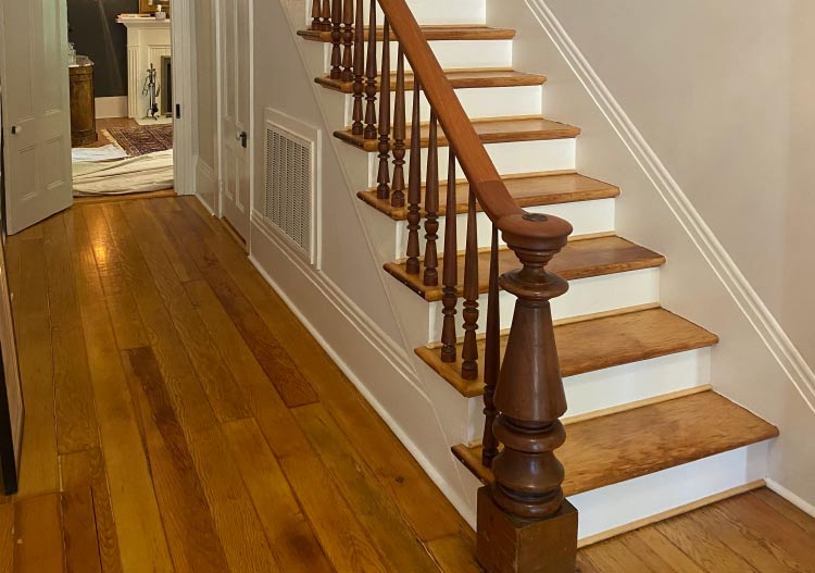 Historic home entrance and staircase showing the successful restoration and refinishing of original wide-plank pine wood flooring and matching dark wood bannister