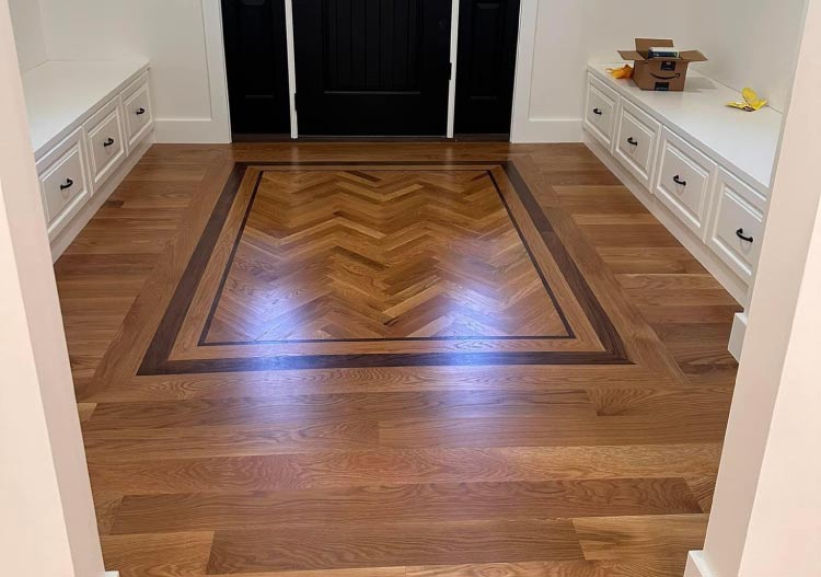Stunning entryway floor featuring a custom herringbone pattern inlay surrounded by a dark walnut border and light oak planks, completed after hardwood floor refinishing in folsom, ca