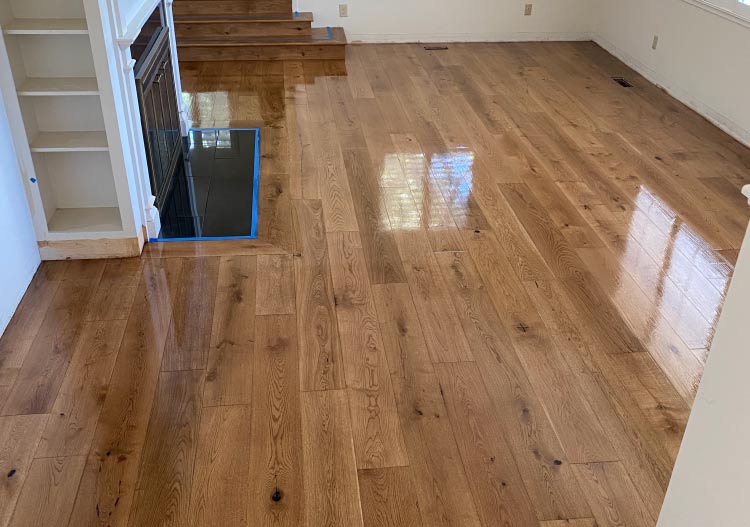 Newly refinished light-to-medium brown character-grade oak plank flooring with a semi-gloss protective finish, next to a built-in bookshelf and stairs