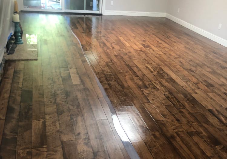 In-progress shot of dark, wide-plank maple wood floor refinishing, showing the contrast between the newly applied wet, glossy finish and the sanded, unsealed portion