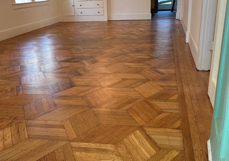 Parquet or mosaic patterned wood floor after expert refinishing, highlighting the intricate geometric design and the restoration of aged wood grain in a residential setting