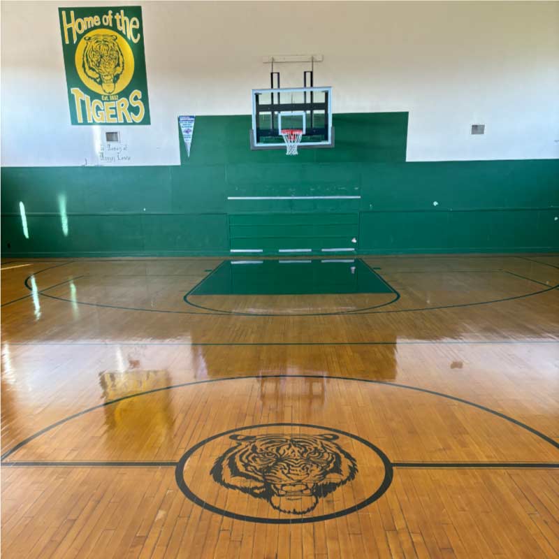 A large, well-maintained basketball court with a polished wooden floor, painted lines, and two basketball hoops