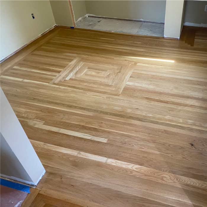 A room with a newly installed light-colored hardwood floor featuring a geometric inlay design in the center