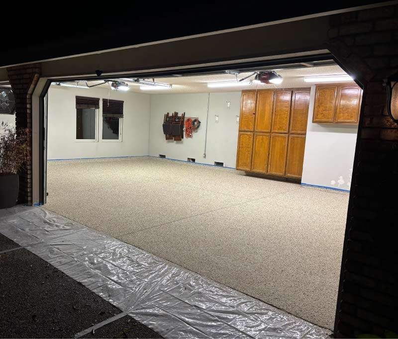 Full view of a residential garage transformation in the Sacramento Valley showing the application of a high-performance epoxy floor coating with protective plastic masking and industrial-grade finish