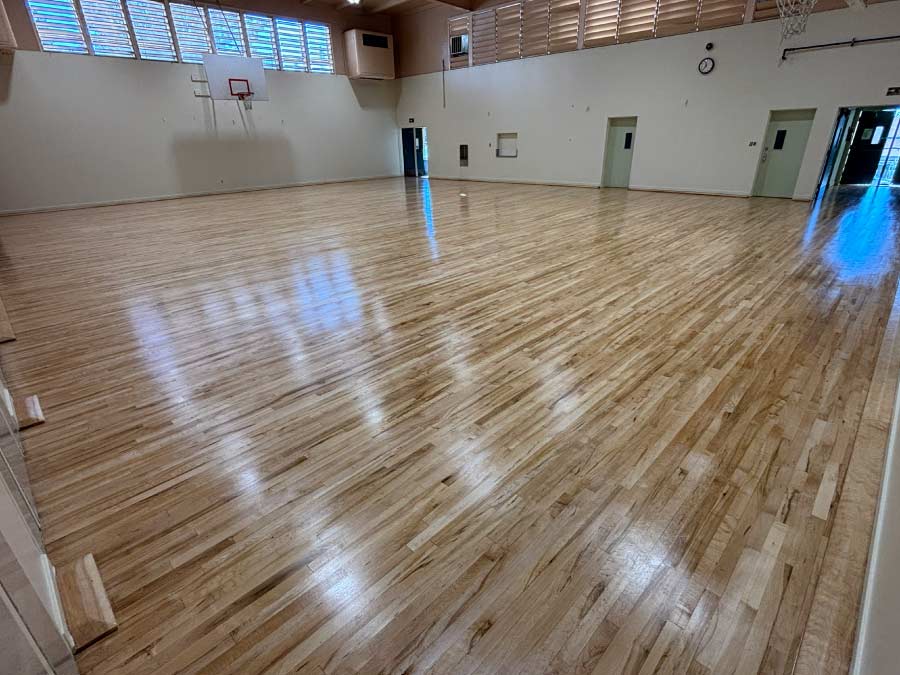 Expansive high school gymnasium after a complete hardwood floor restoration, displaying a flawless, durable finish suitable for high-impact sports.