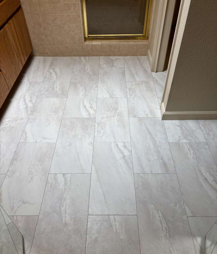 High-end luxury vinyl tile (LVT) installation in a bathroom, featuring a waterproof stone-look marble pattern with clean grout lines and expert fitting around vanity cabinets and doorways.