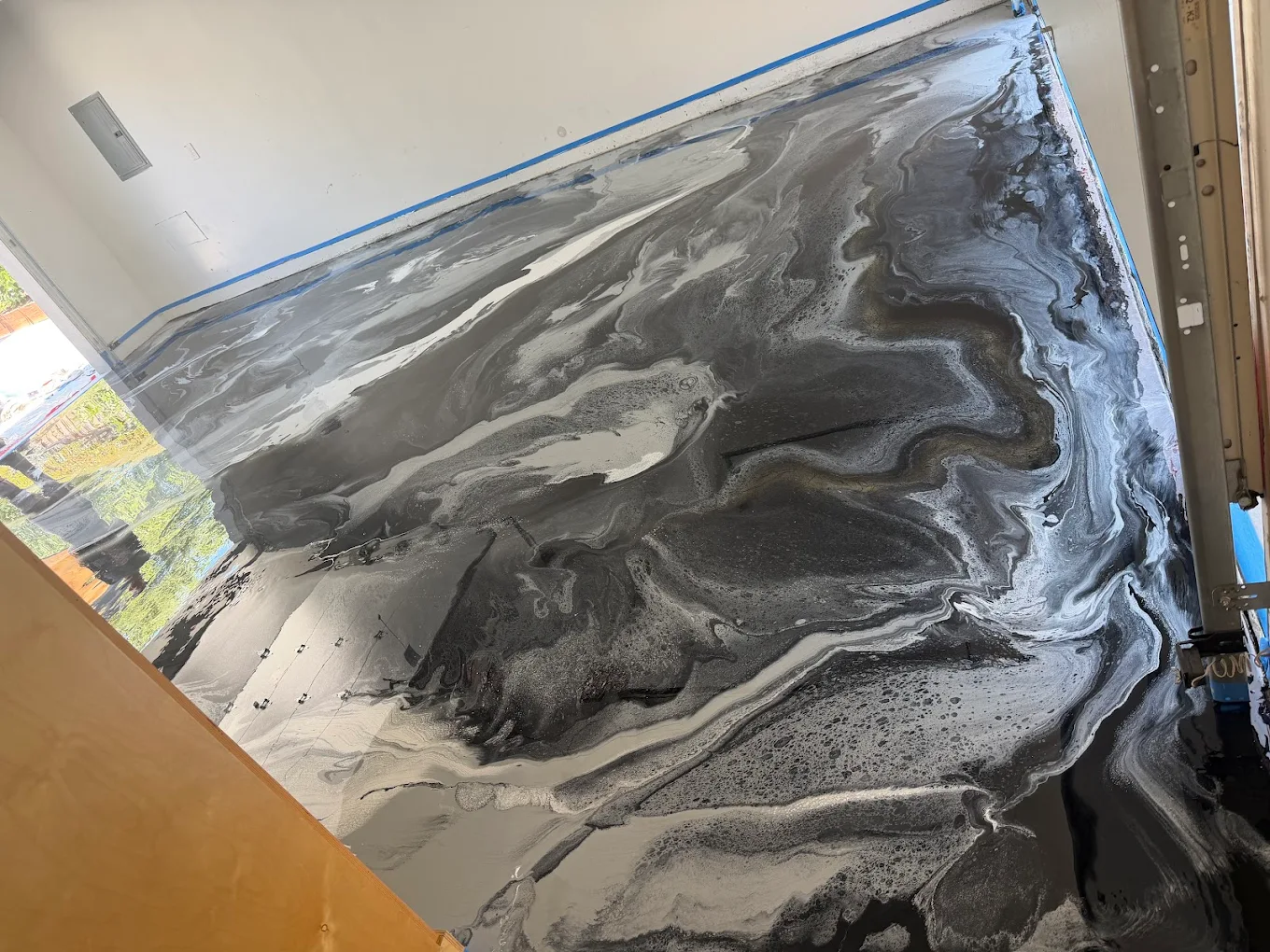 High-end custom metallic epoxy floor application featuring a luxurious, liquid swirling marble design in deep charcoal, silver, and white hues.