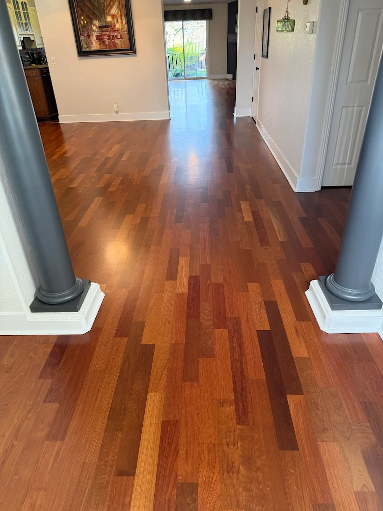 Elegant multi-toned cherry hardwood floor installation running through an open-concept home layout, framed by modern dark grey architectural pillars.